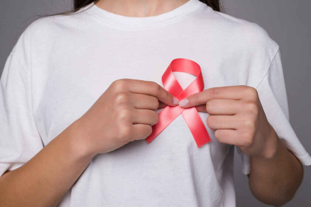 World Breast Cancer Day Concept. Health care woman wore white t-shirt with red ribbon for awareness. Symbolic bow color raising on people living with women’s breast tumor illness World Breast Cancer Day Concept. Health care woman wore white t-shirt with red ribbon for awareness. Symbolic bow color raising on people living with women’s breast tumor illness