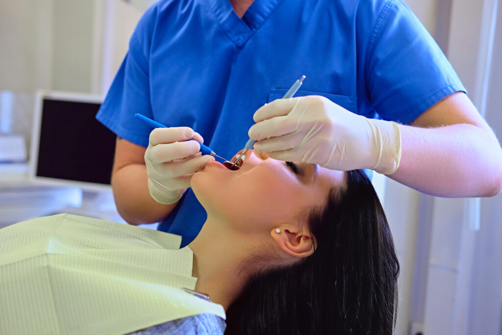 Dentist examining female’s teeth in dentistry.