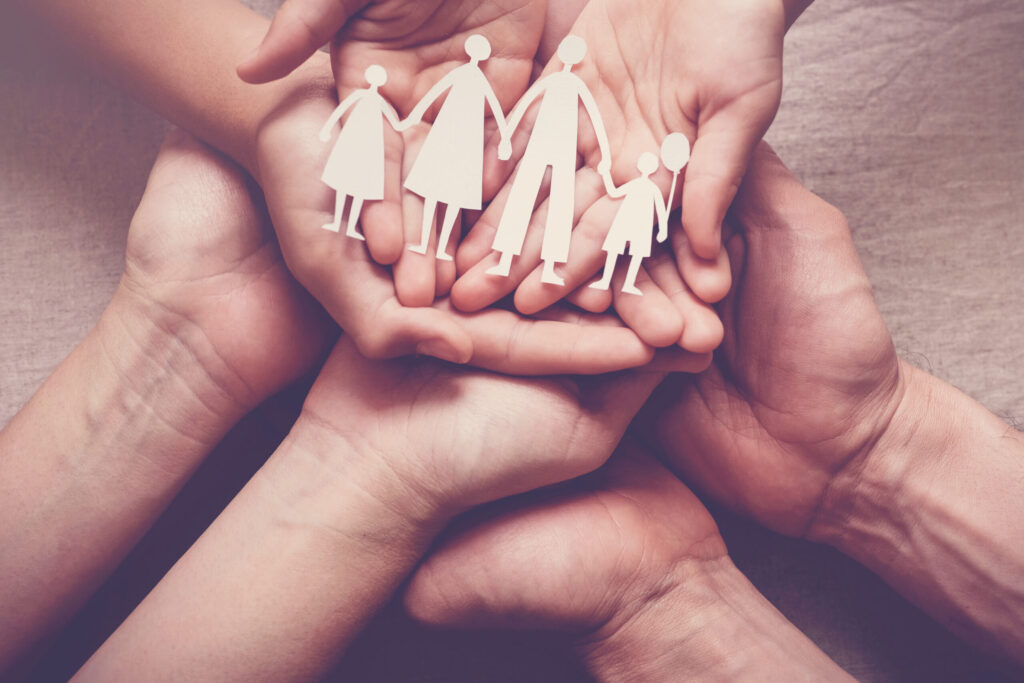 Adult and children hands holding paper family cutout, family hom