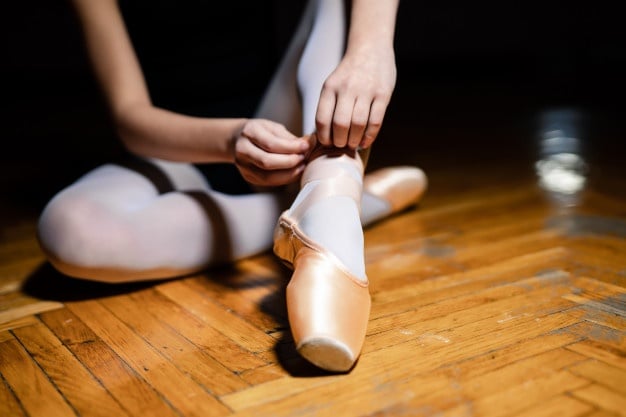 bailarina-sentada-no-chao-de-madeira-e-amarrar-as-sapatilhas-antes-do-treino-bailarina-amarra-seus-argumentos-fechar-se_116317-920