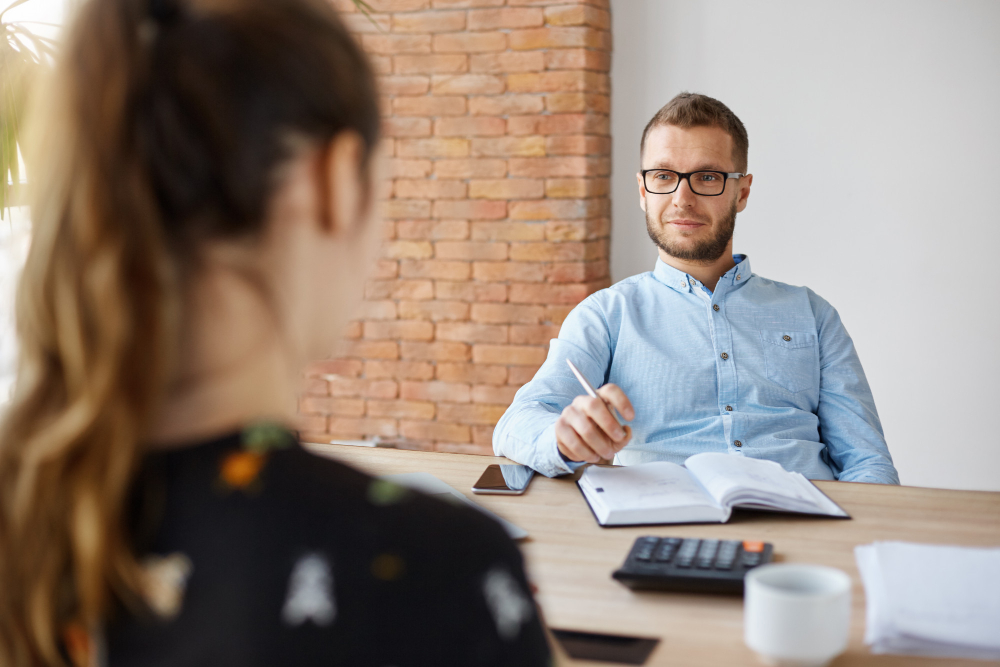 business-concept-job-interview-adult-bearded-male-hr-manager-in-glasses-and-shirt-sitting-in-light-office-in-front-of-brunette-caucasian-woman-asking-questions-about-previous-work-place-1