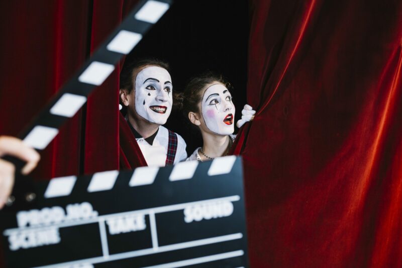clapperboard-in-front-of-excited-mime-couple-peeking-behind-the-red-curtain-min-scaled-e1645116252392
