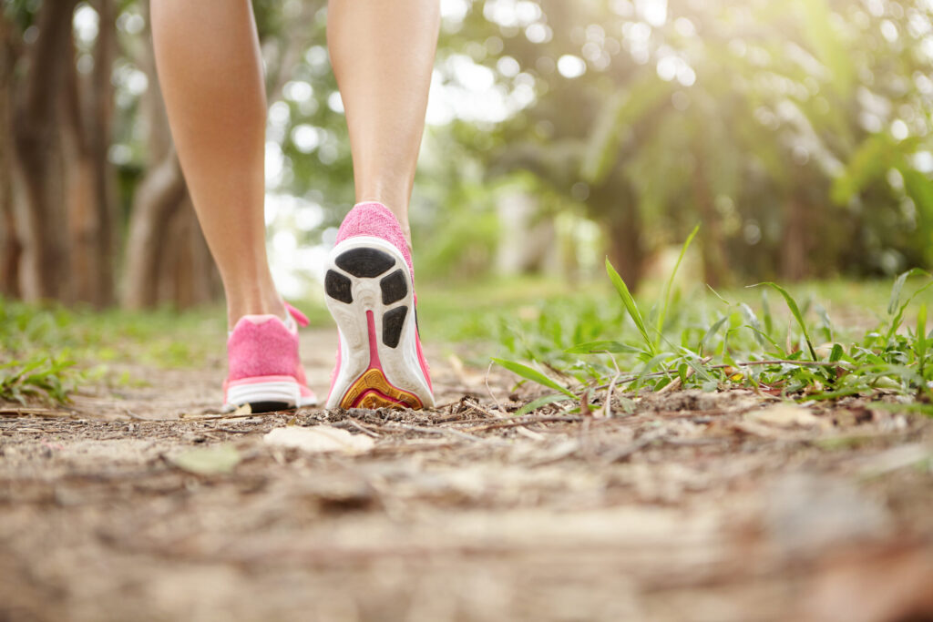 Cropped shot of athlete girl in pink running shoes hiking in forest on sunny day. Fit slim legs of sporty female in sneakers during jogging workout. Selective focus on sole. Shallow depth of field Cropped shot of athlete girl in pink running shoes hiking in forest on sunny day. Fit slim legs of sporty female in sneakers during jogging workout. Selective focus on sole. Shallow depth of field