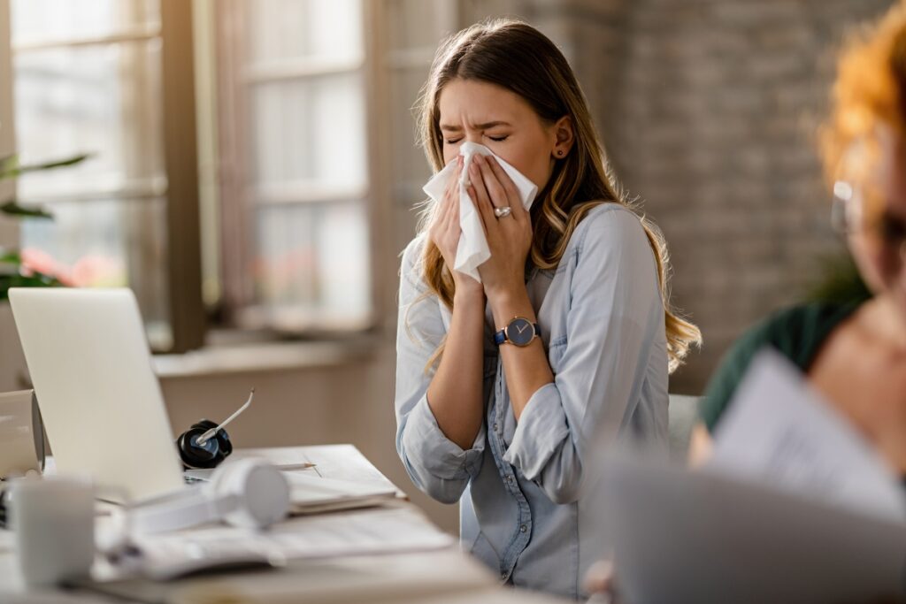 Young sick businesswoman sneezing in a tissue while working in the office. doencas-inverno