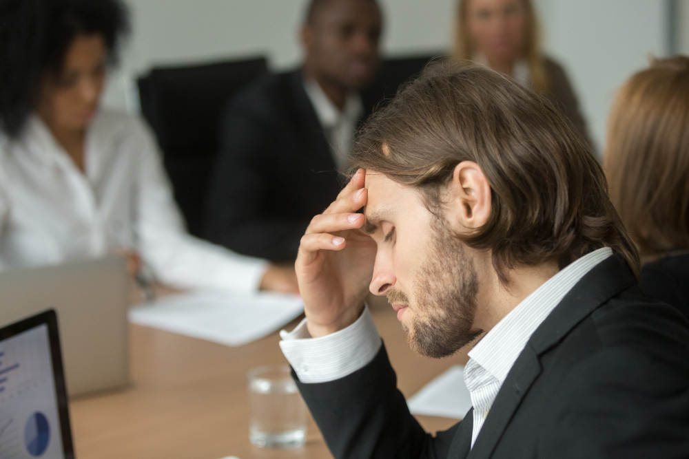 frustrated-tired-businessman-having-strong-headache-at-diverse-team-meeting