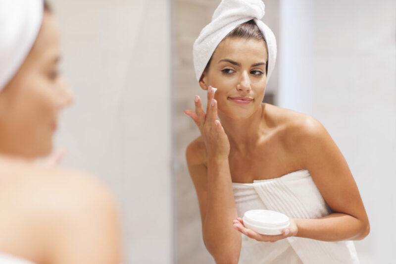 Gorgeous woman applying moisturizer on face