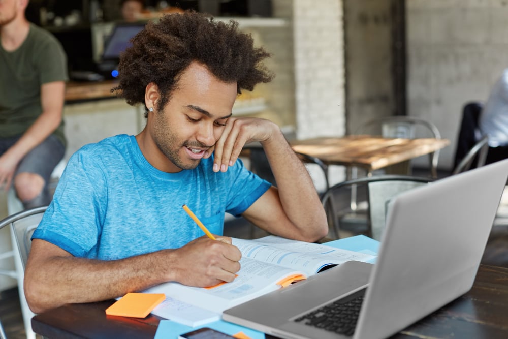 hardworking-african-american-graduate-a-student-dressed-casually-making-notes-with-pencil-in-textbook-while-looking-for-information-for-course-paper-surfing-high-speed-internet-on-laptop-pc hardworking-african-american-graduate-a-student-dressed-casually-making-notes-with-pencil-in-textbook-while-looking-for-information-for-course-paper-surfing-high-speed-internet-on-laptop-pc