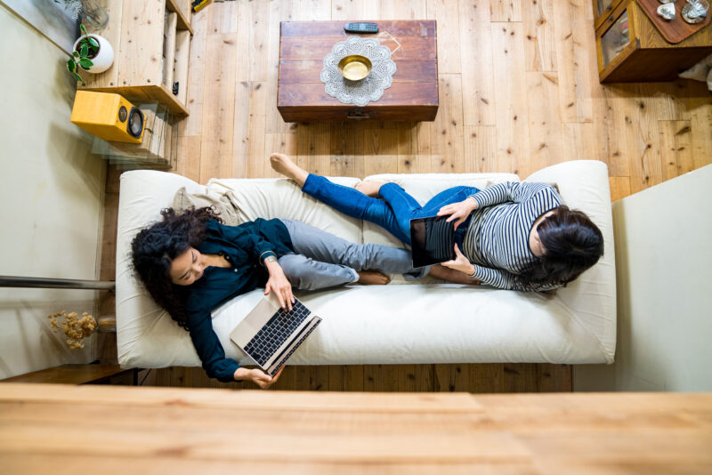 Mother and daughter laying on the sofa using smart devices