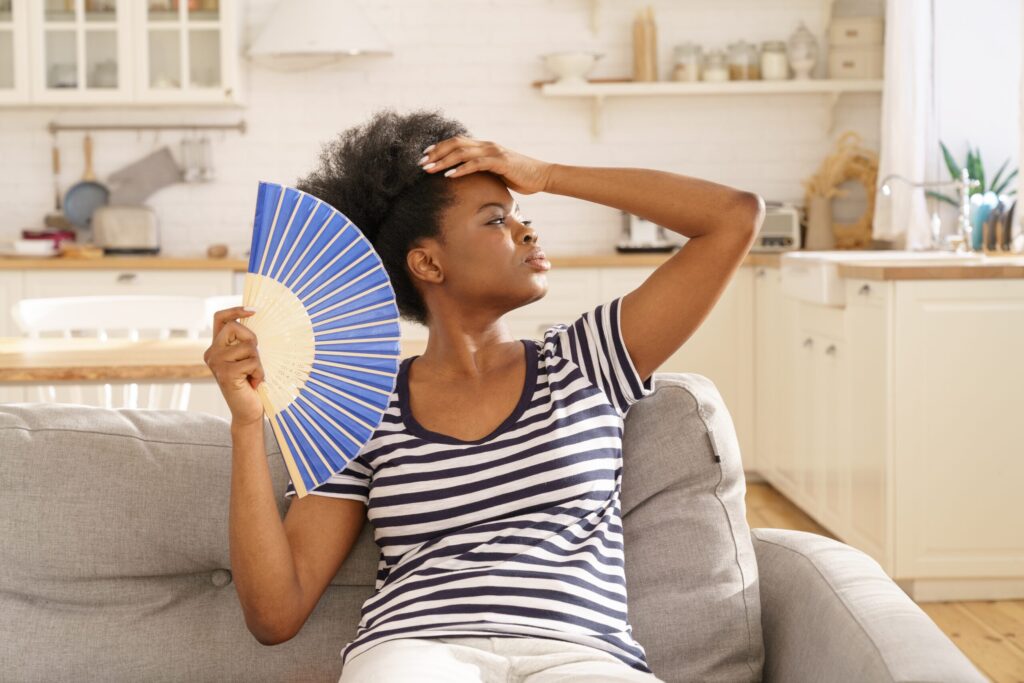 Millennial black woman suffer from heatstroke, hot temperature at home use paper fan for fresh air
