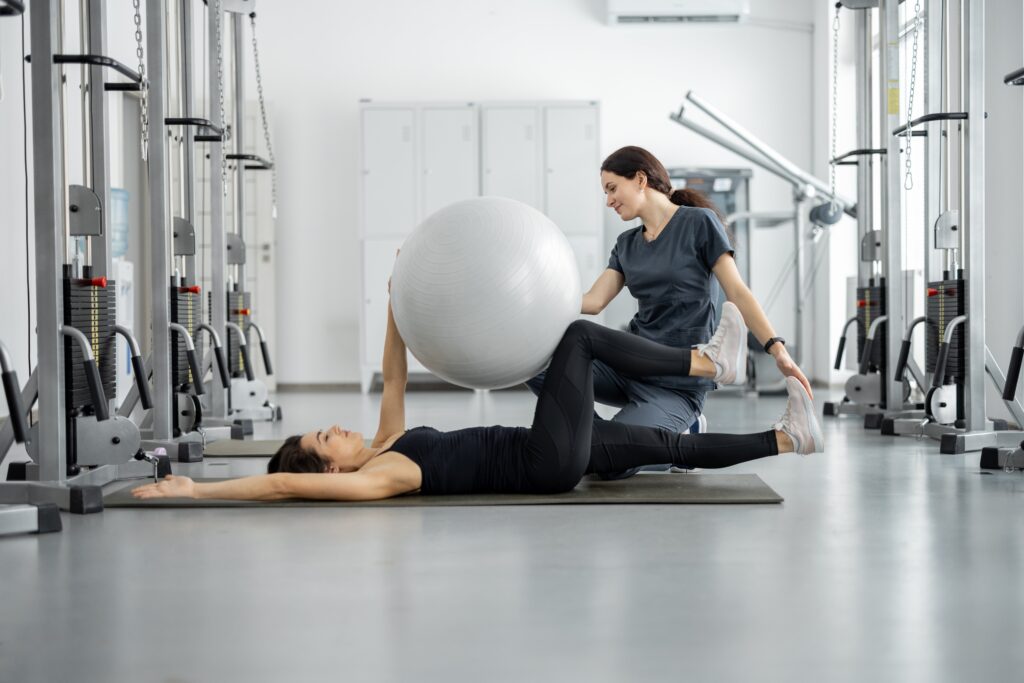 Woman doing exercises with fitness ball with rehabilitation specialist at the gym