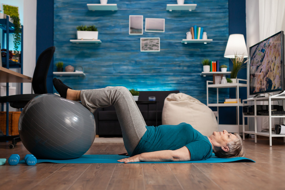 retired-senior-woman-doing-practicing-legs-up-exercise-using-swiss-ball-sitting-on-yoga-mat