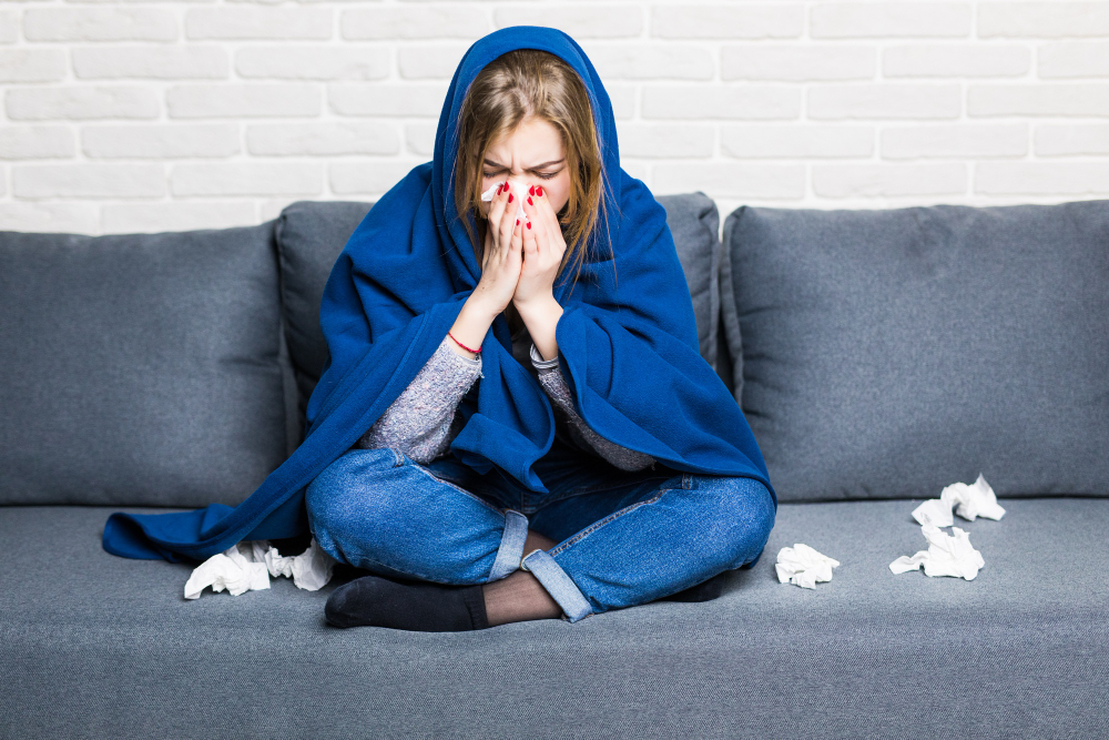 sick-woman-with-rheum-and-headache-holding-napkin-sitting-on-sofa-with-coverlet-and-pills-at-home