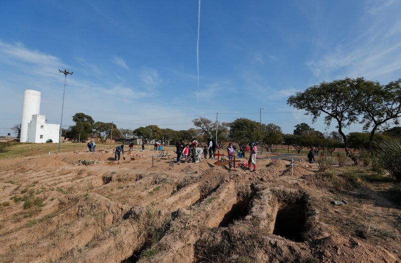 Parentes de mortos pela Covid-19 ao lado de novas valas abertas em cemitério de Córdoba, na Argentina