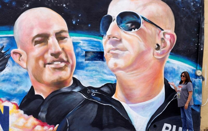 Mulher posa para foto em frente a mural de Jeff Bezos e seu irmão Mark, em Van Horn