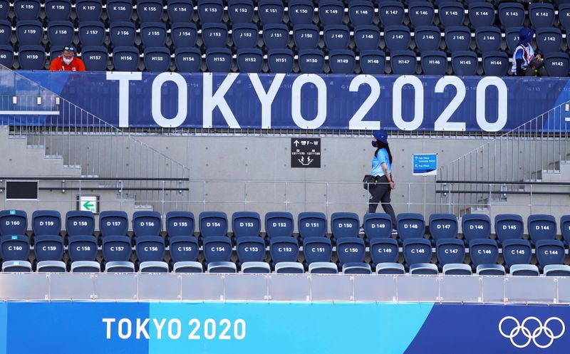 Espectadora caminha embaixo de placa da Tóquio 2020 no estádio onde é disputado o torneio olímpico do hóquei