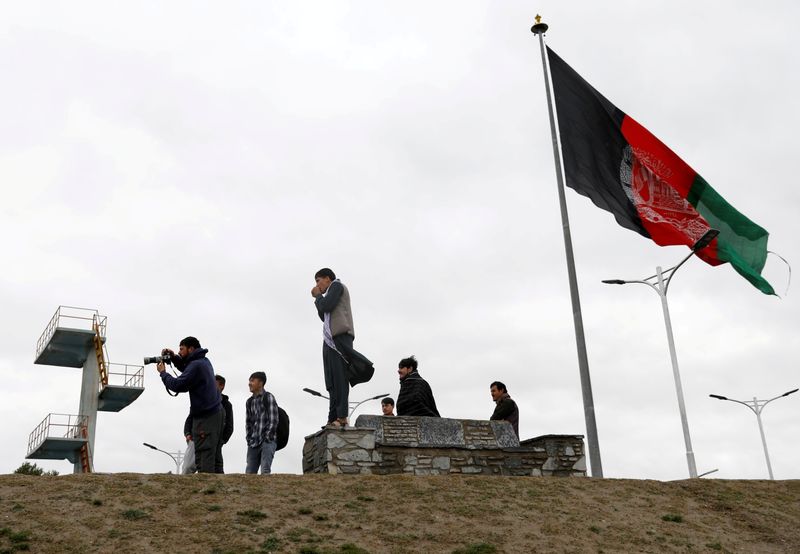 Pessoas tiram fotos ao lado da bandeira afegã em Cabul