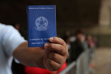 Pessoa mostra carteira de trabalho em fila de emprego em São Paulo