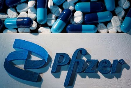 Logo da Pfizer ao lado de comprimidos fabricados pela farmacêutica em foto de ilustração