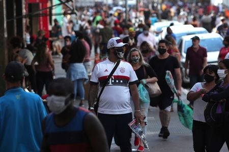 Pedestres usando máscaras caminham em rua comercial de São Paulo