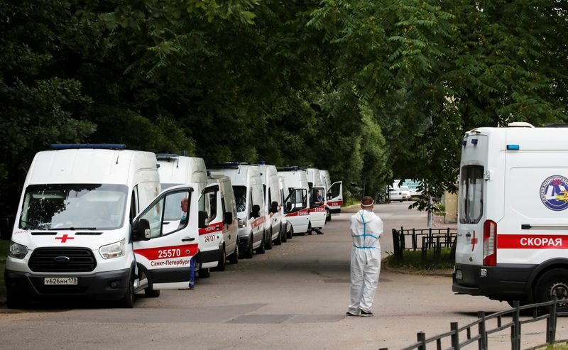 Profissional de saúde em trajes de proteção ao lado de ambulâncias estacionadas do lado de fora de hospital em São Petersburgo, na Rússia