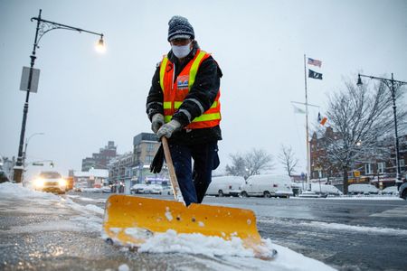 Funcionário limpa neve de calçada do lado de fora de estação de metrô no Brooklyn, em Nova York