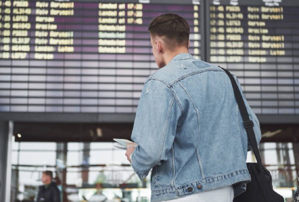 Homem esperando voo no aeroporto em frente ao painel de informações