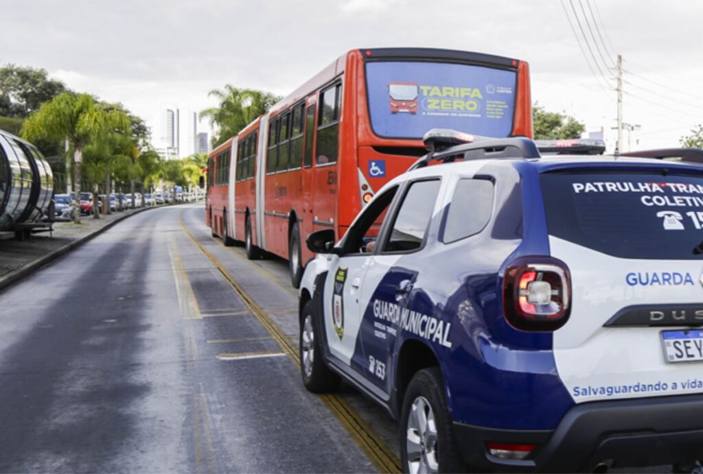 Viatura da guarda municipl atrás de ônibus biarticulado.