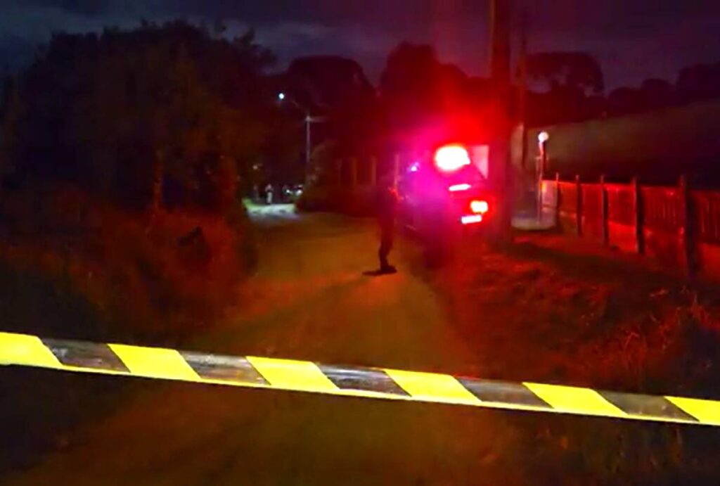 Fita zebrada com viatura do IML ao fundo com as sirenes acesas