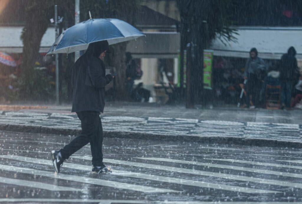 Homem com guarda-chuva atravessando a rua