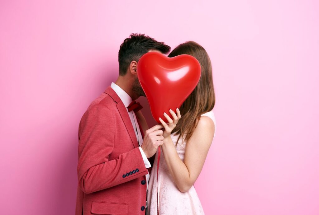 Casal abaixonado atrás de um balão de coração.