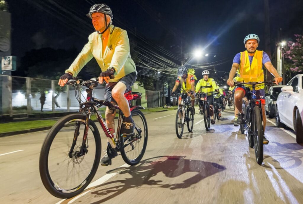 Grupo de ciclistas pedalando na rua a noite.