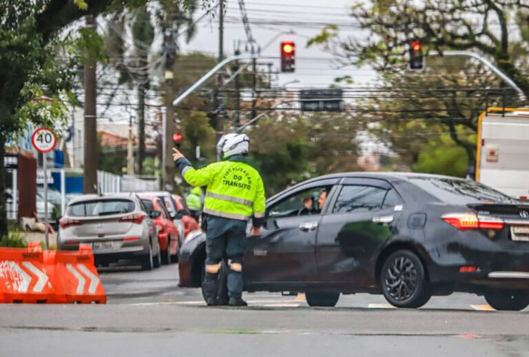 Guarda rodoviário orientando um carro em rua bloqueada.