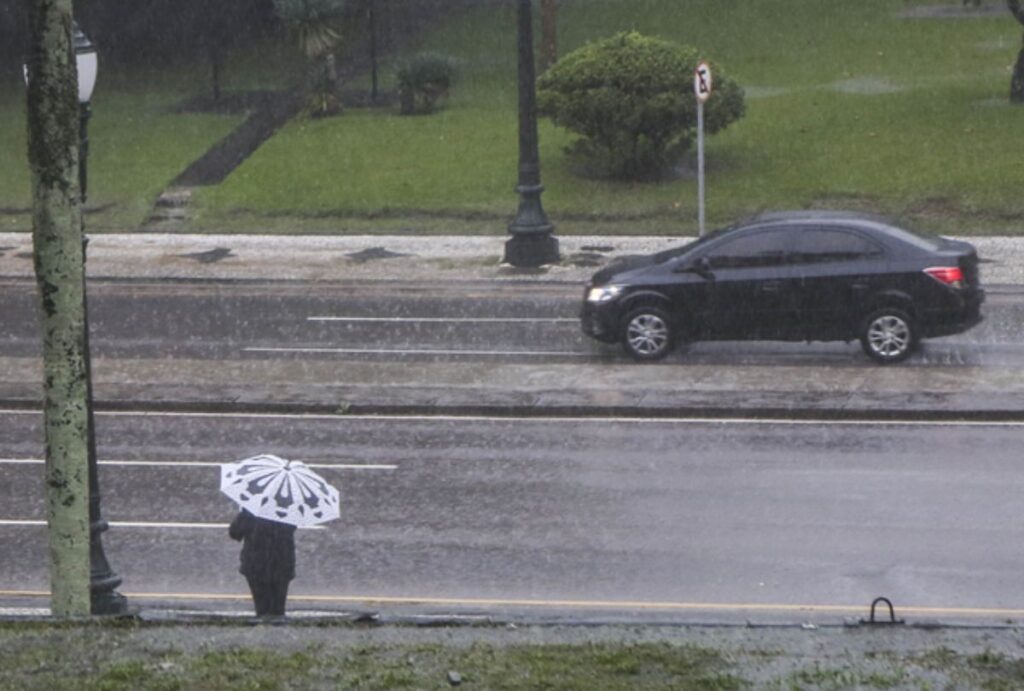 Pessoa segurando um guarda-chuva enquanto um carro passa na rua
