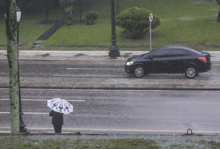 Pessoa segurando um guarda-chuva enquanto um carro passa na rua