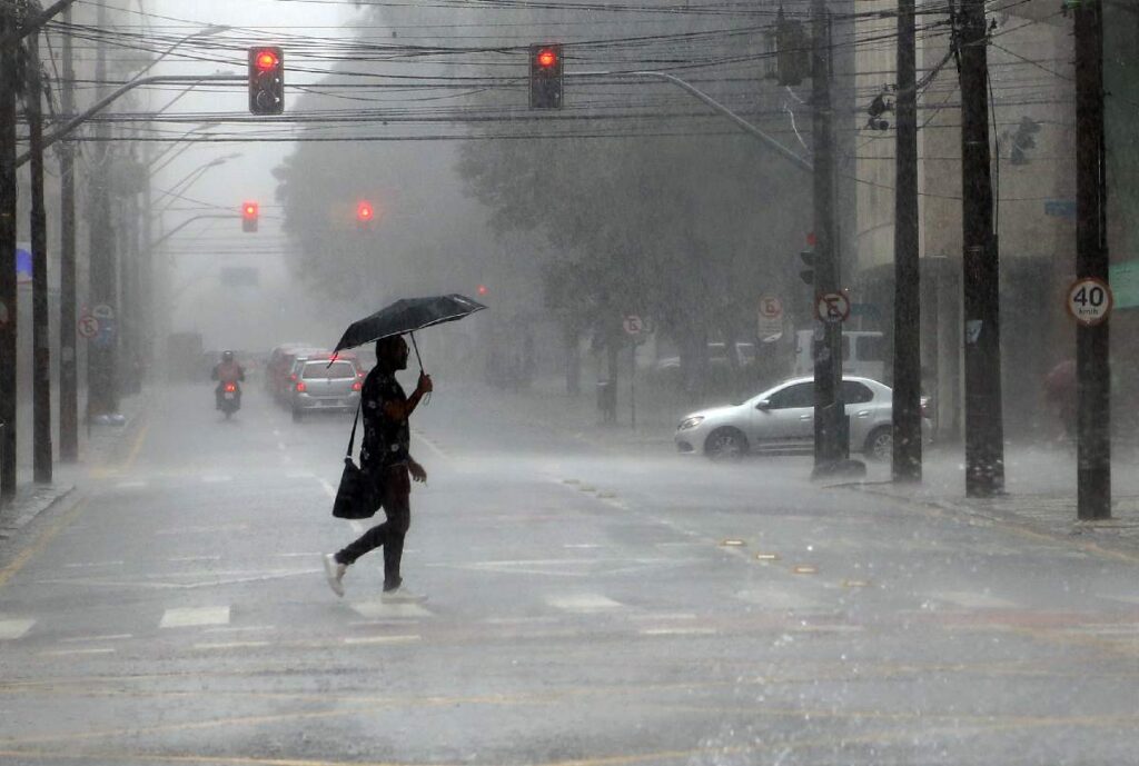 Homem atravessando a rua durante uma chuva, com um guarda-chuva