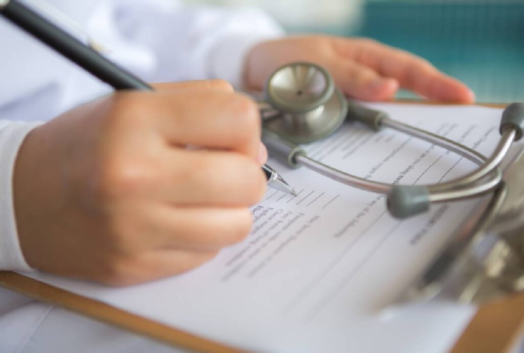Estetoscópio em cima de prancheta e médico fazendo anotações