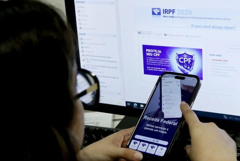 Pessoa mexendo no celular na frente de um computador