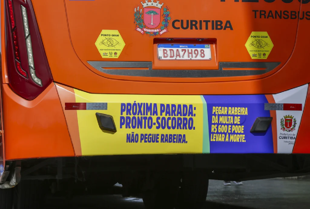 Placa na parte de trás de um ônibus alertando os riscos de pegar rabeira